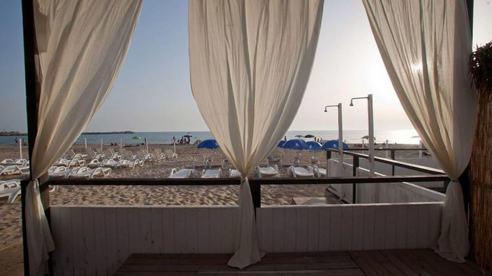 Gazebo con tende bianche sulla spiaggia con vista mare al tramonto
