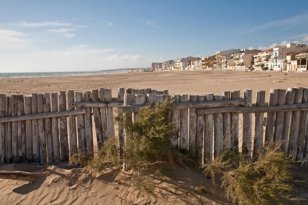 Lunga spiaggia di sabbia con staccionata in legno e case sullo sfondo