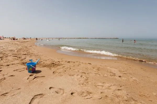 Spiaggia di sabbia dorata con secchiello e mare calmo