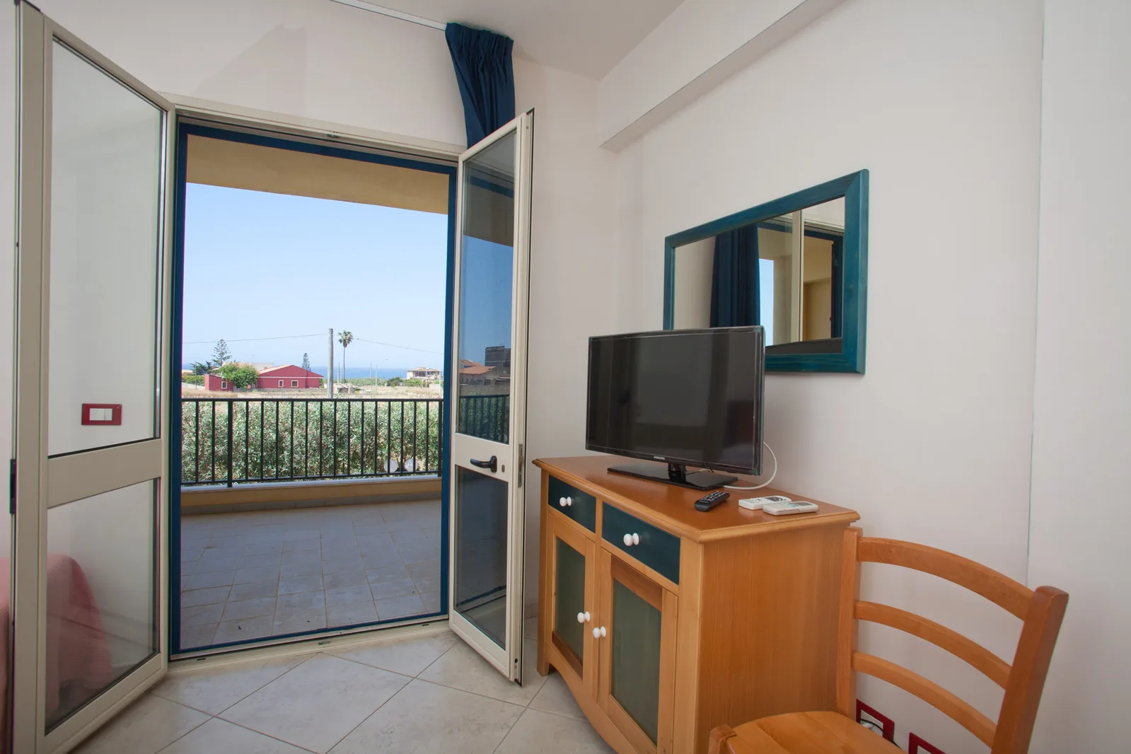 Soggiorno con TV, mobile in legno e porta finestra sul balcone con vista mare