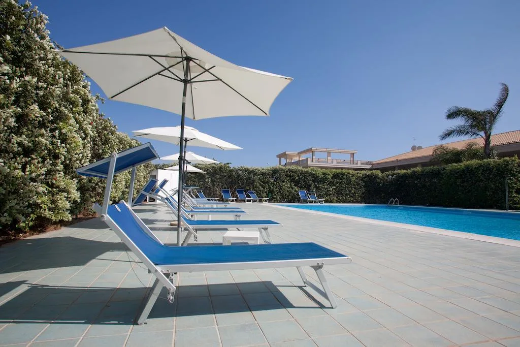 Piscina con lettini blu e ombrelloni bianchi circondata da siepi