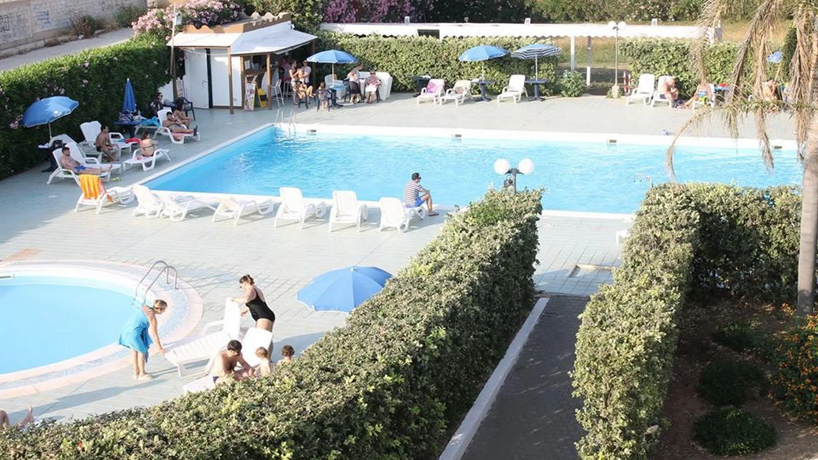Piscina con lettini, ombrelloni e bar bordo piscina con ospiti