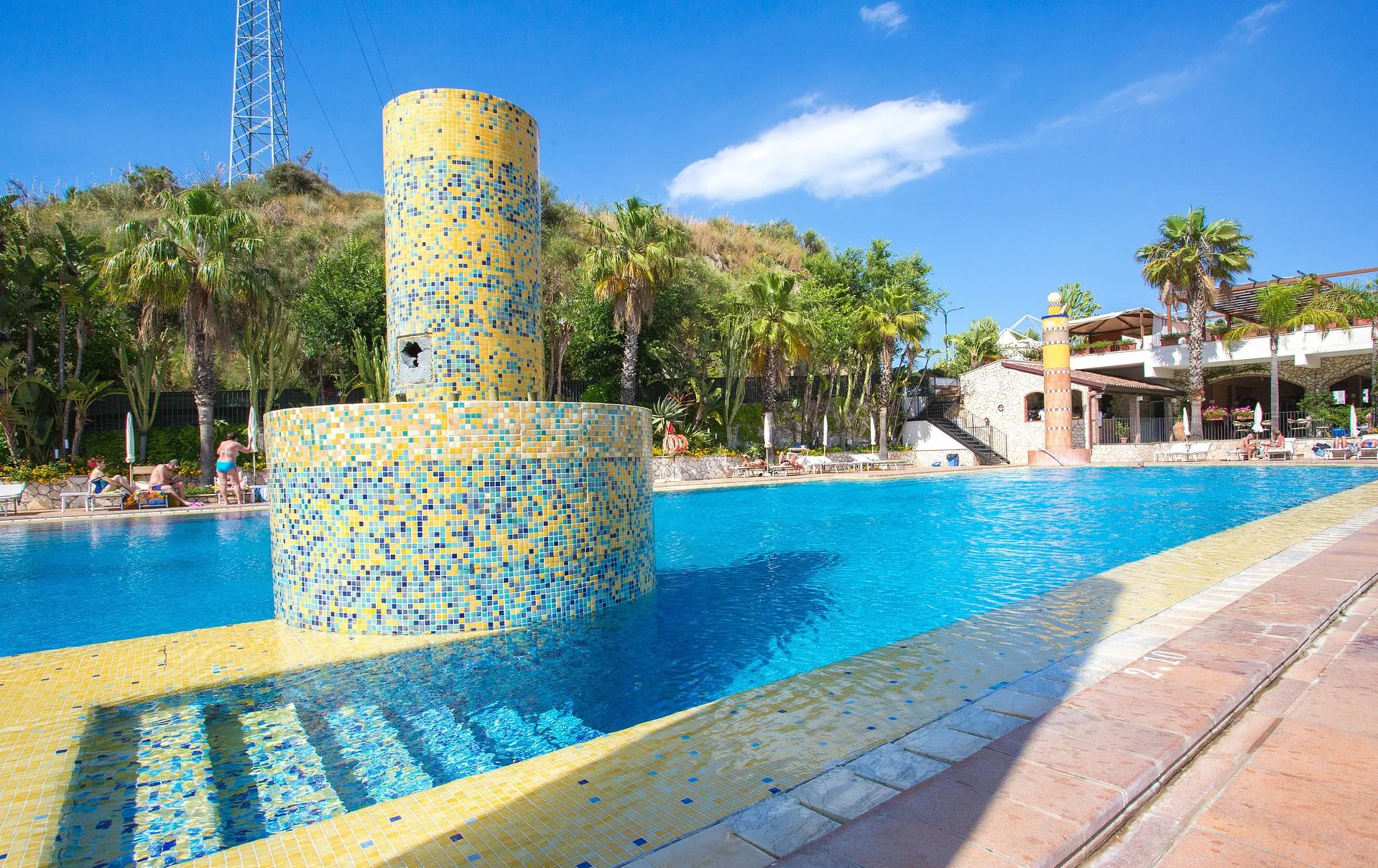 Piscina con fontana a mosaico e palme sotto il cielo azzurro