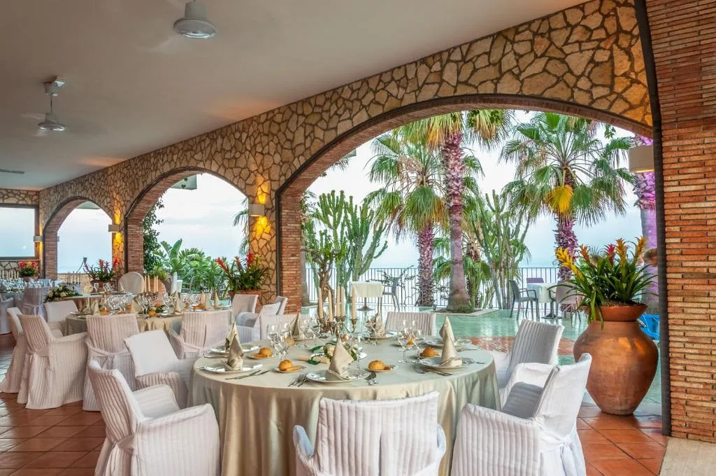 Sala ristorante elegante con tavoli allestiti sotto archi in pietra e palme