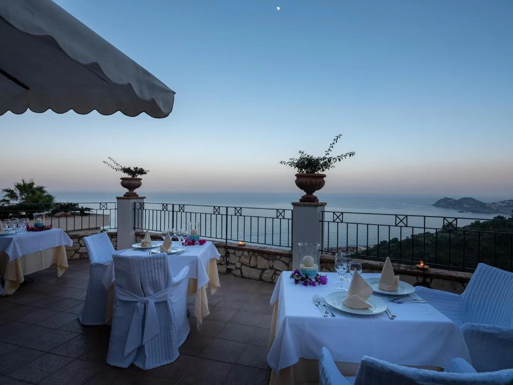 Tavoli del ristorante allestiti su terrazza al tramonto con vista sul mare