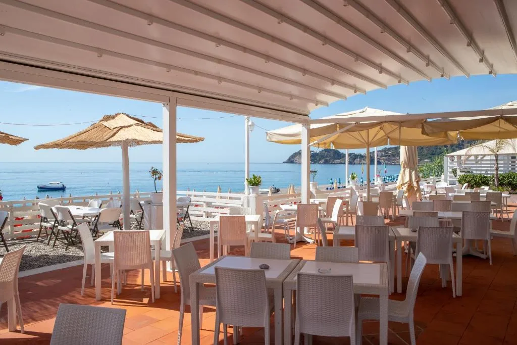 Terrazza ristorante coperta con tavoli bianchi e vista sulla spiaggia e sul mare