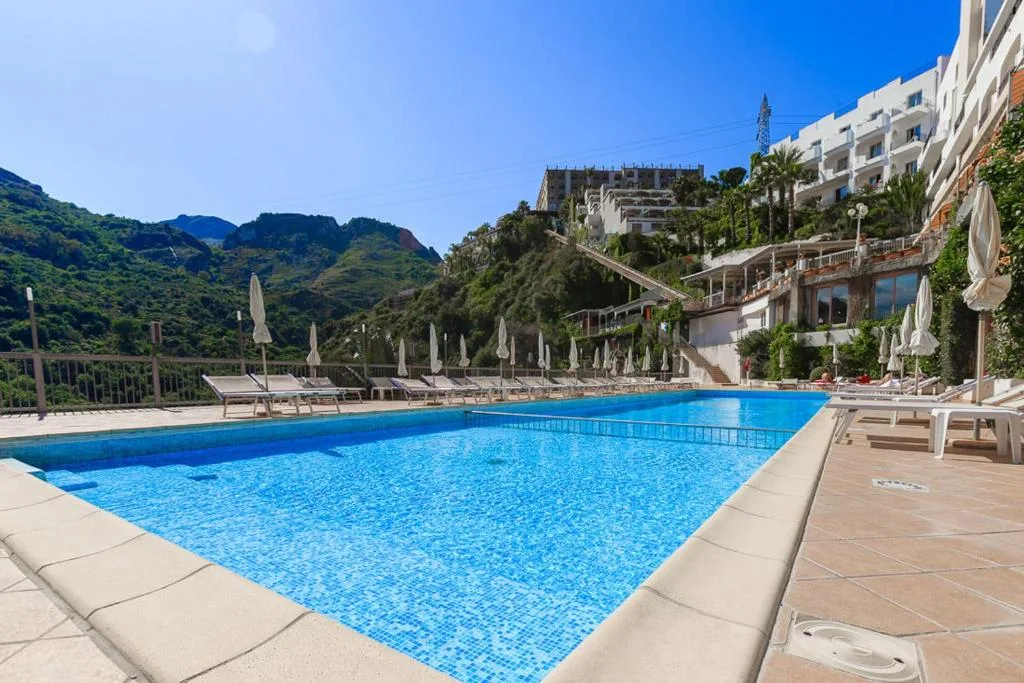Piscina azzurra con lettini e ombrelloni chiusi e vista sulle montagne