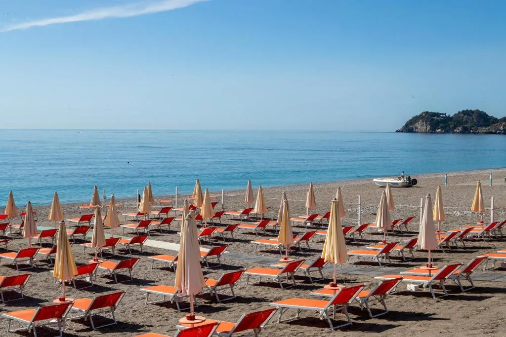 Spiaggia con lettini arancioni e ombrelloni allineati davanti al mare