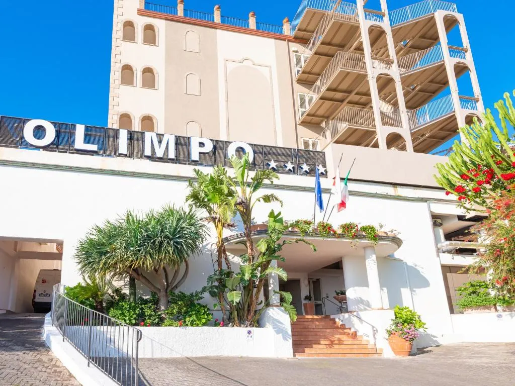 Ingresso dell'Hotel Olimpo con insegna, piante e bandiere
