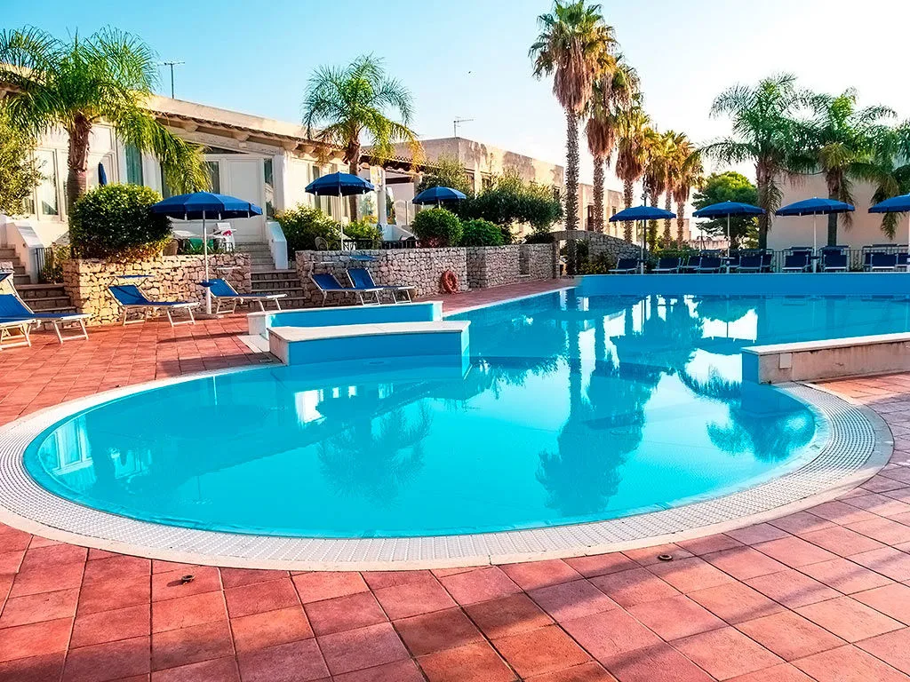 Piscina con bordo arrotondato circondata da palme e ombrelloni