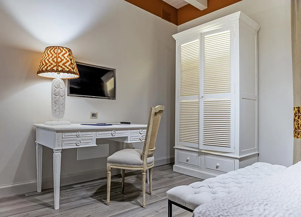 Angolo scrivania in camera con armadio bianco, sedia imbottita e lampada decorativa