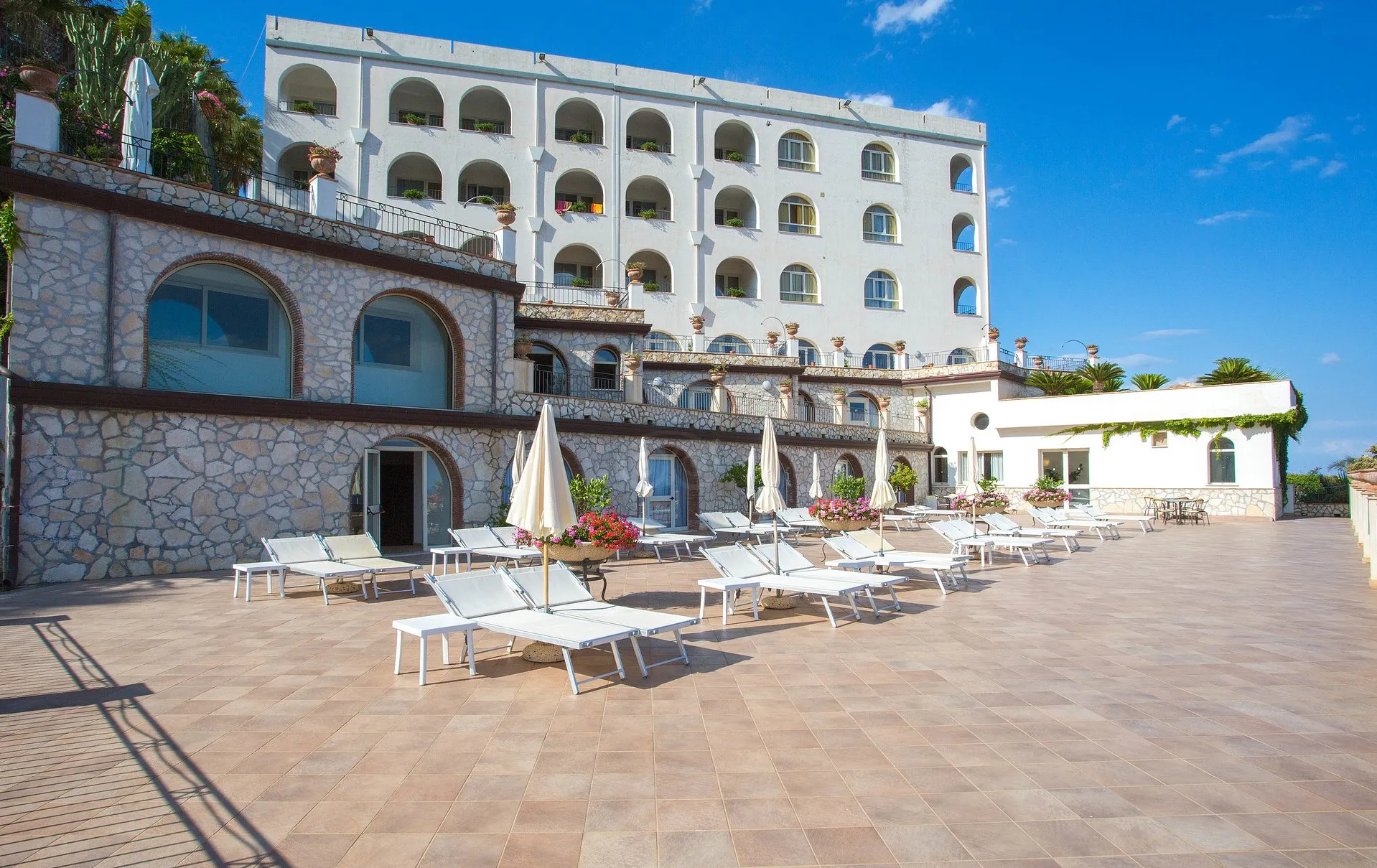 Facciata dell'hotel con terrazza, lettini e ombrelloni bianchi