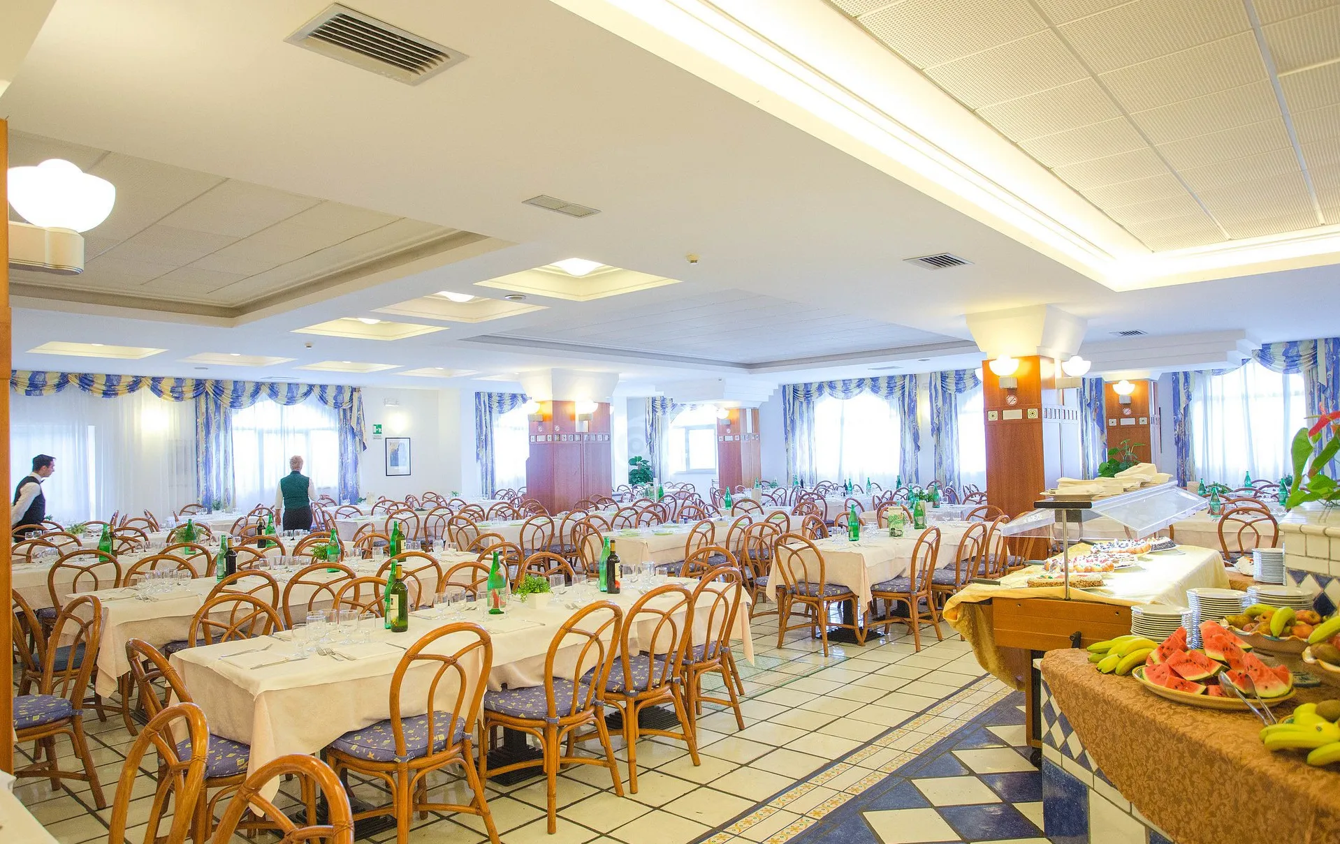 Ampia sala ristorante con tavoli apparecchiati e buffet di frutta