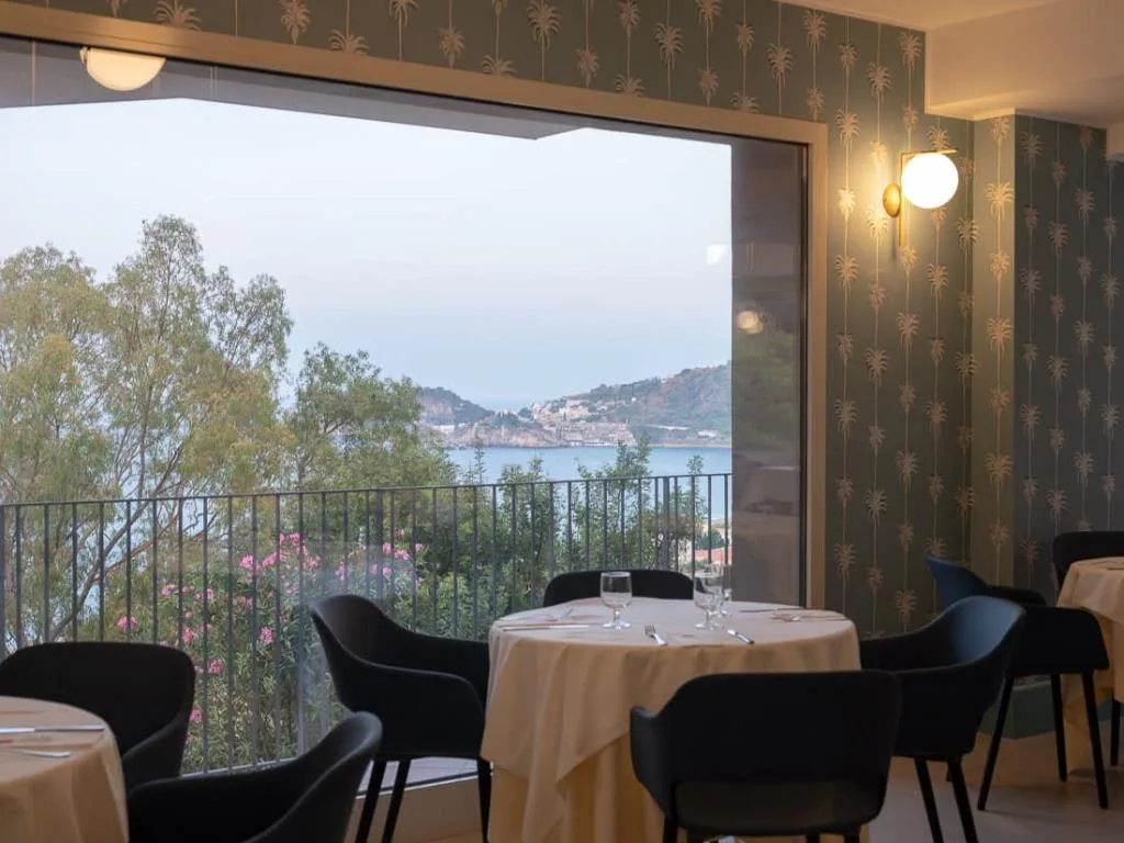 Sala ristorante con grande vetrata affacciata sul mare e sulla vegetazione