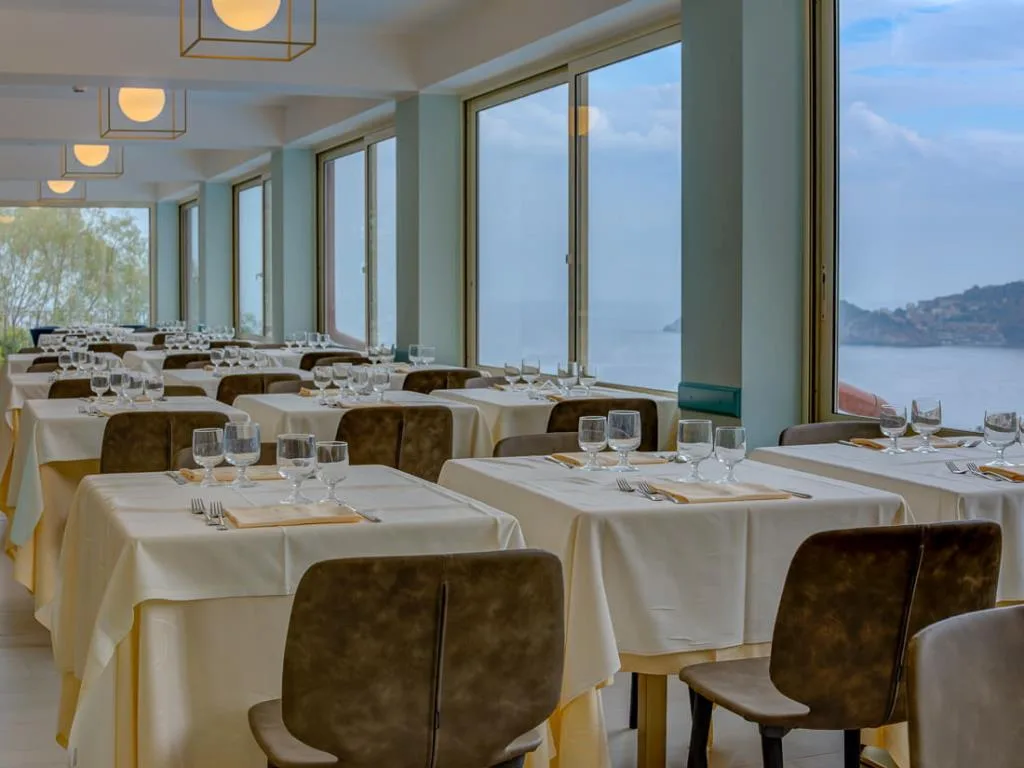 Sala ristorante luminosa con ampie vetrate affacciate sul mare