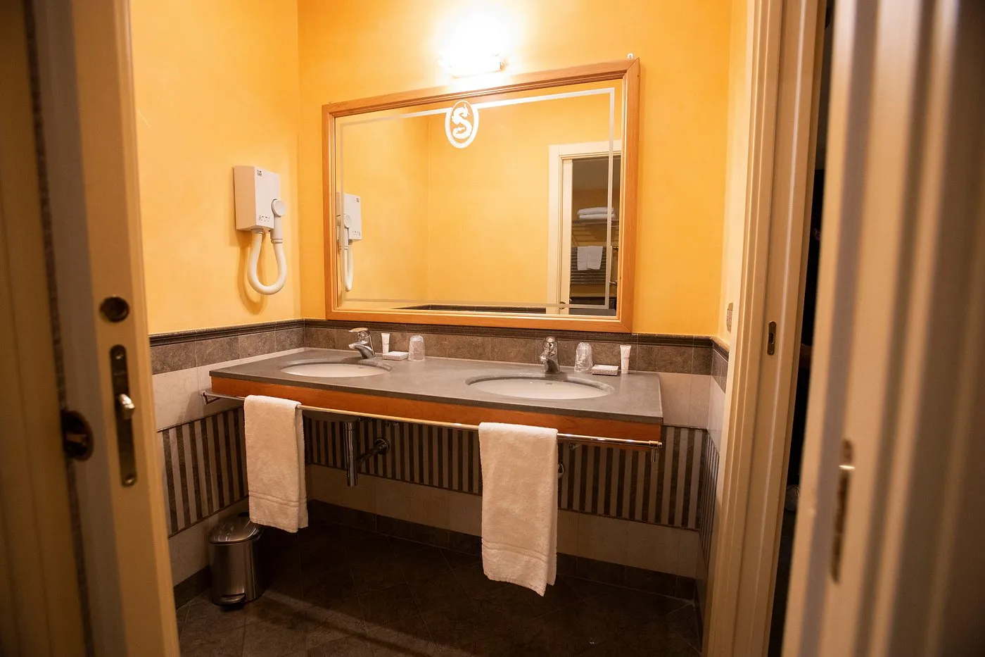 Bagno della camera con doppio lavabo, specchio e pareti gialle