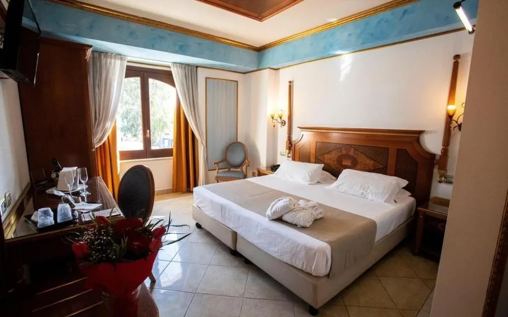 Camera classica con testiera intarsiata, accappatoi sul letto e finestra luminosa