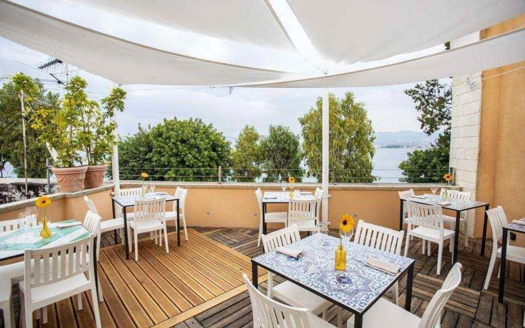 Terrazza ristorante all'aperto con tavoli, vela ombreggiante e vista sul mare