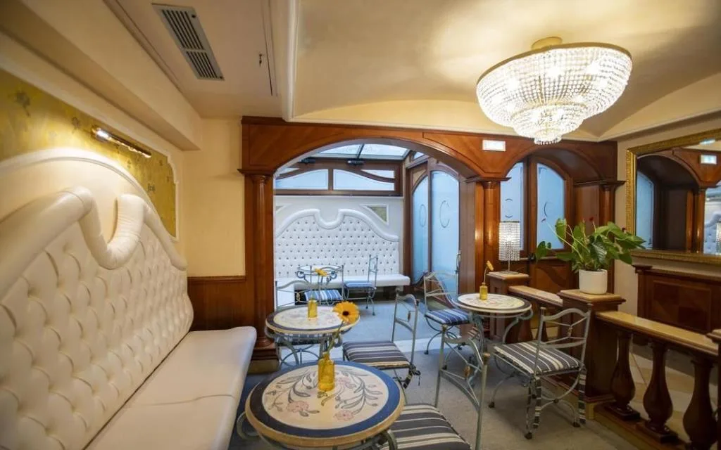 Salottino interno elegante con sedute imbottite bianche, tavolini e lampadario di cristallo
