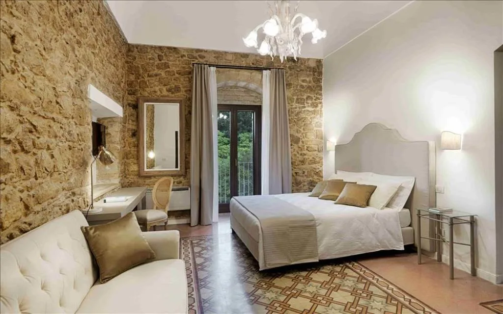 Camera con pareti in pietra, lampadario di vetro, divano bianco e pavimento decorato