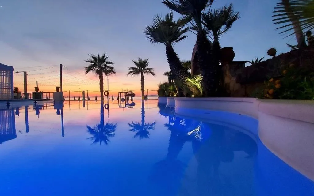 Piscina al tramonto con palme riflesse nell'acqua
