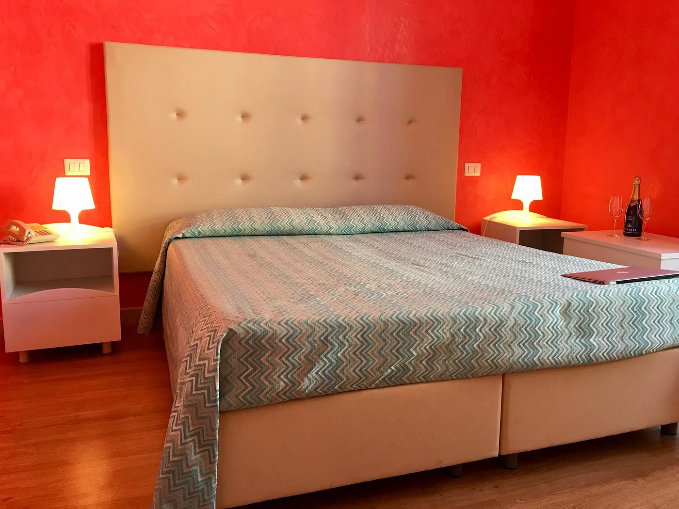 Camera matrimoniale con testiera imbottita, pareti rosse, comodini con lampade e champagne