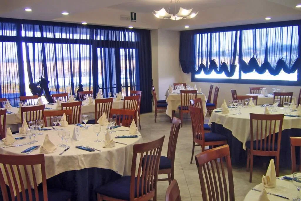 Sala ristorante con tavoli apparecchiati, sedie in legno e ampie vetrate