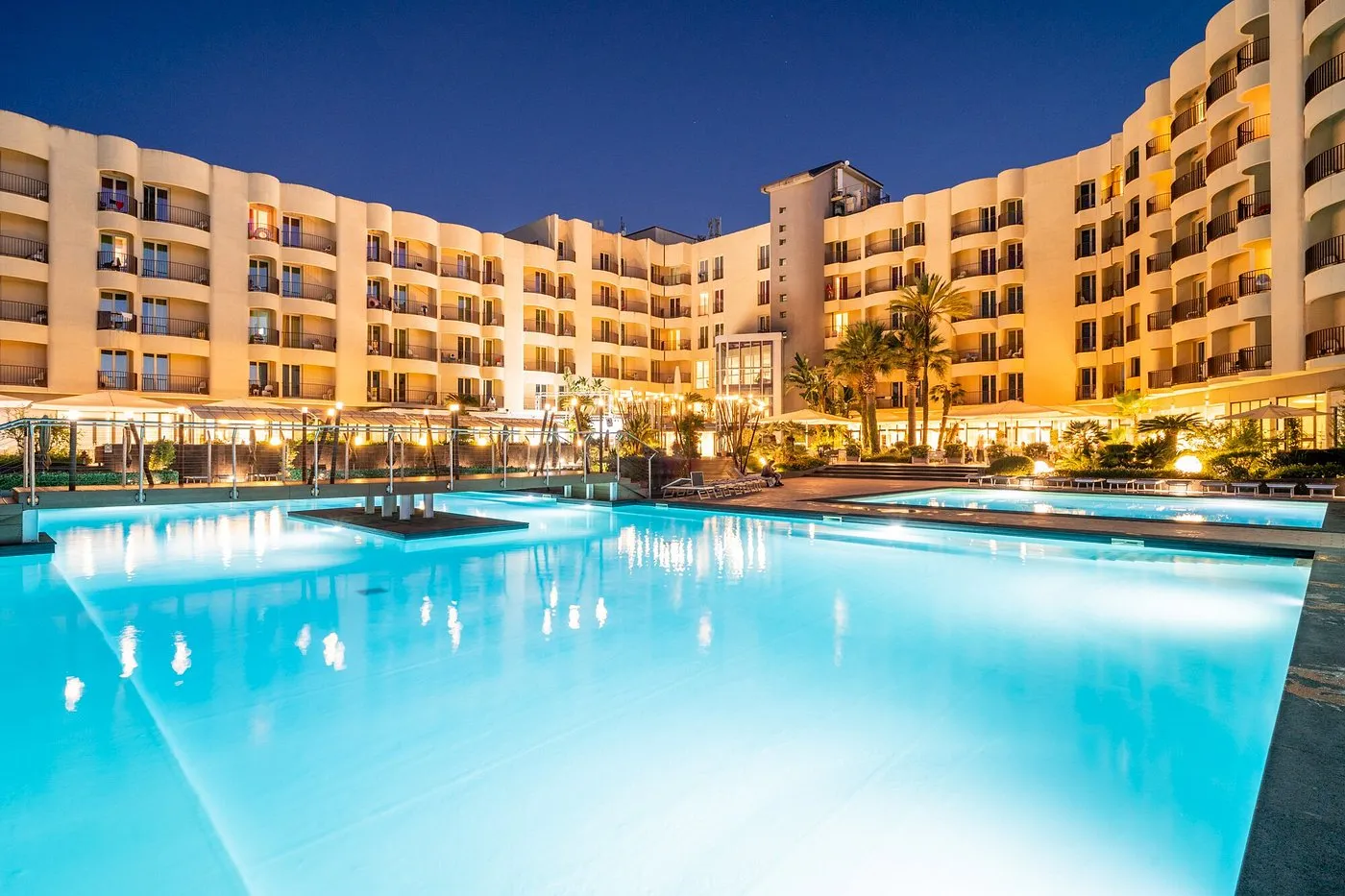 Piscina illuminata al tramonto con edifici del resort sullo sfondo