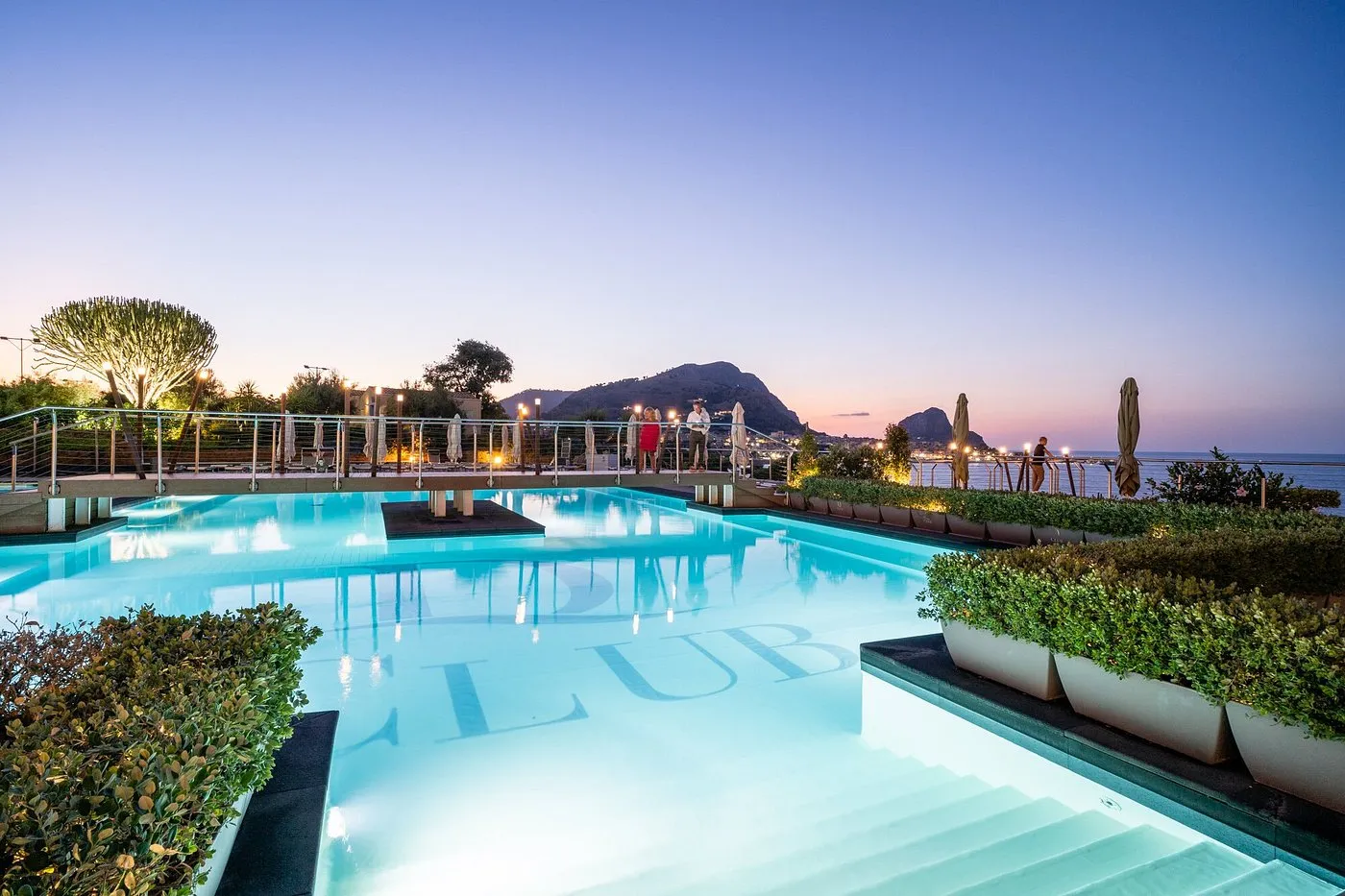 Piscina al crepuscolo con scritta Club e vista panoramica sul golfo al tramonto