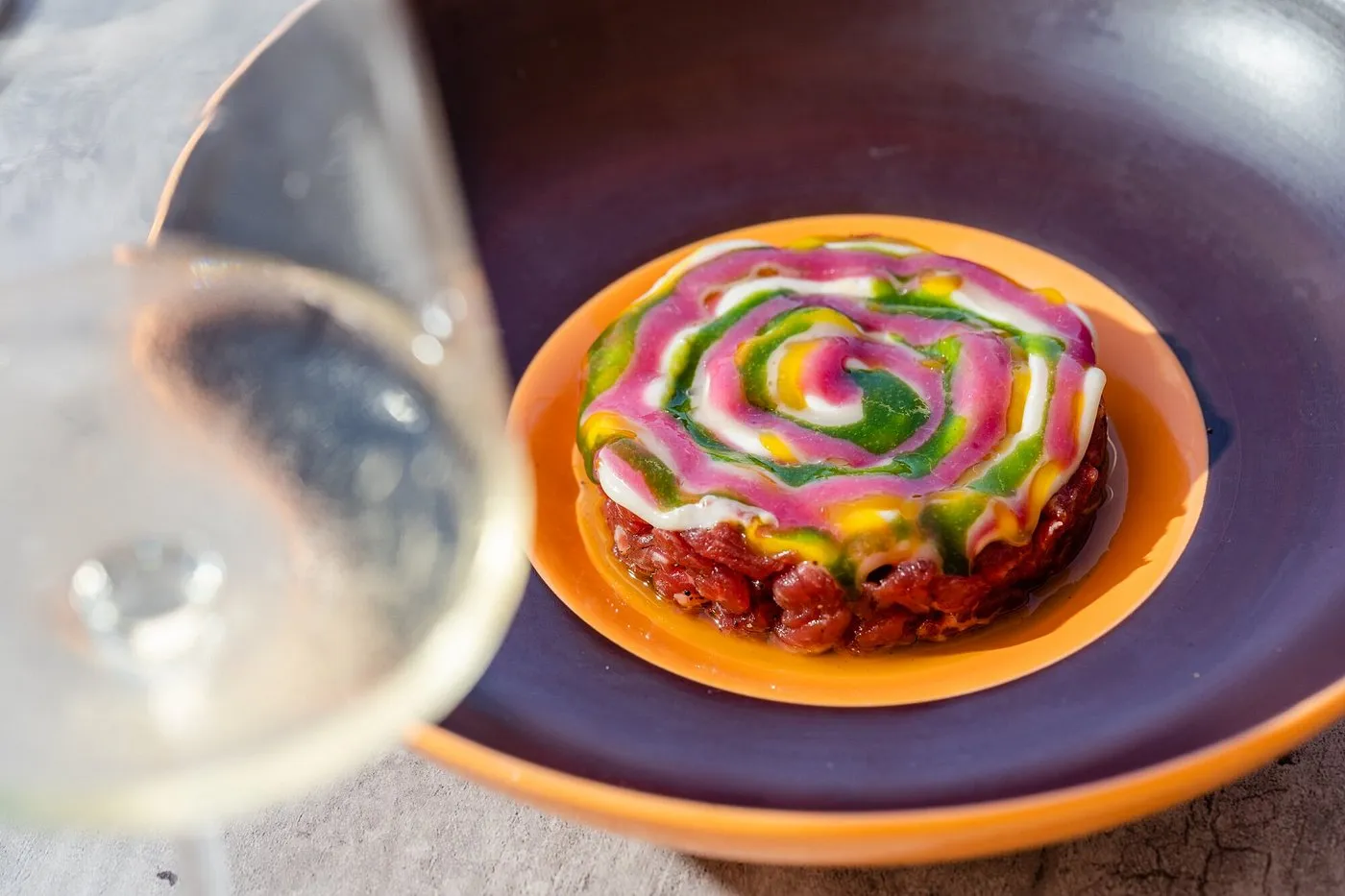 Tartare di carne decorata con salse colorate a spirale e calice di vino bianco