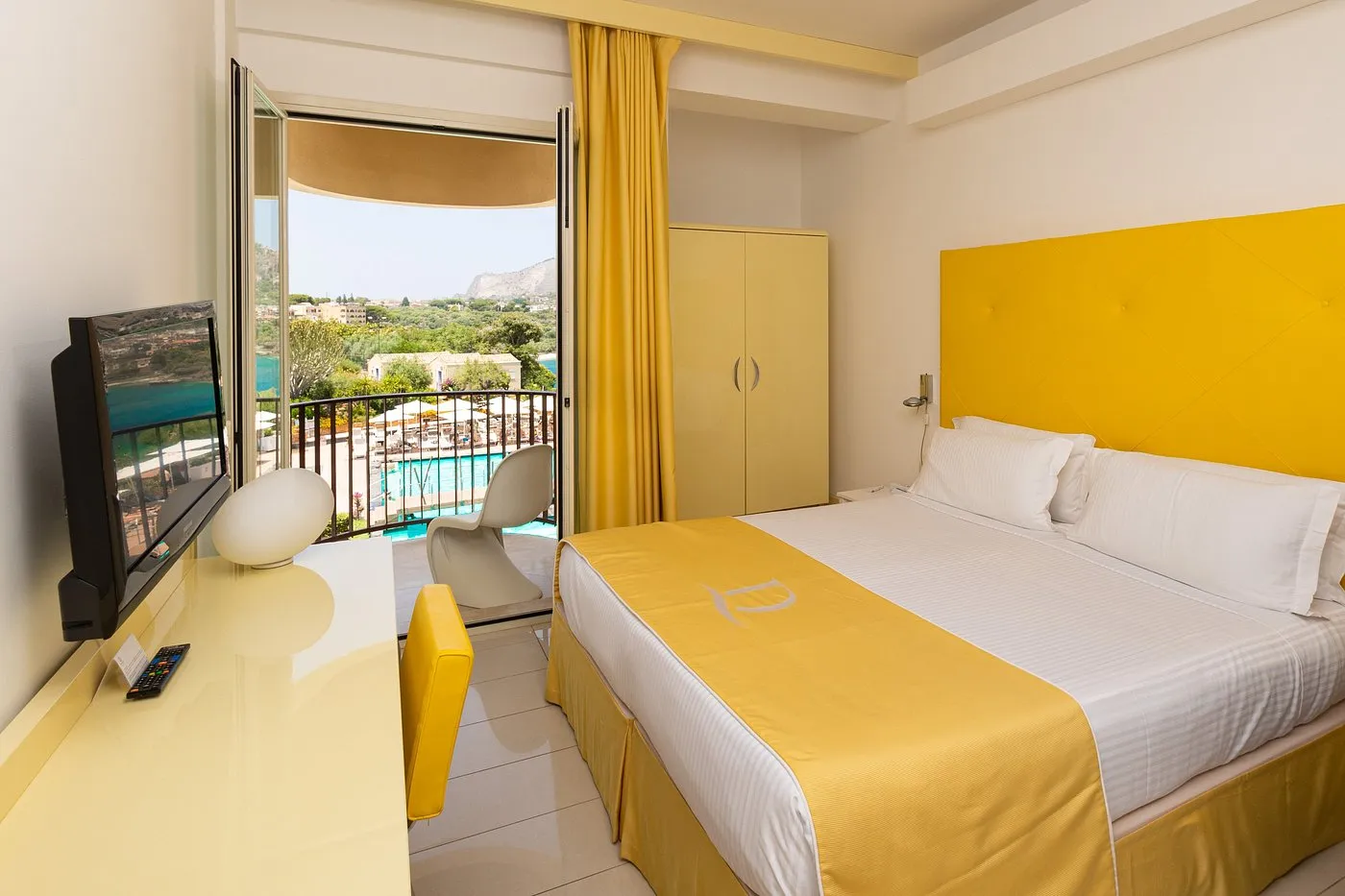 Camera con arredi gialli, letto matrimoniale e balcone con vista sulla piscina e il mare