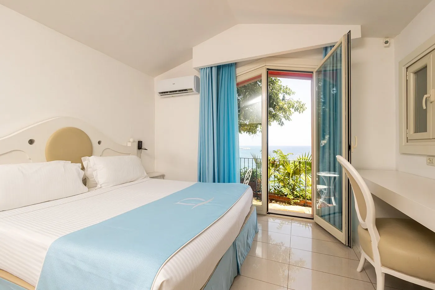 Camera luminosa con letto matrimoniale, biancheria azzurra e balcone con vista mare