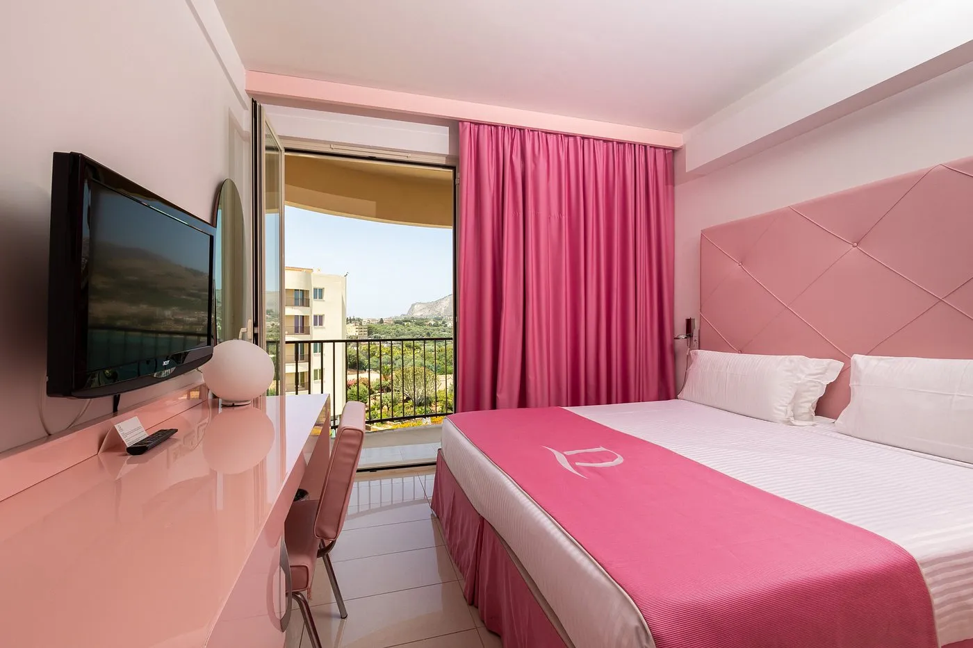 Camera moderna in tonalità rosa con letto matrimoniale, TV e balcone vista collina