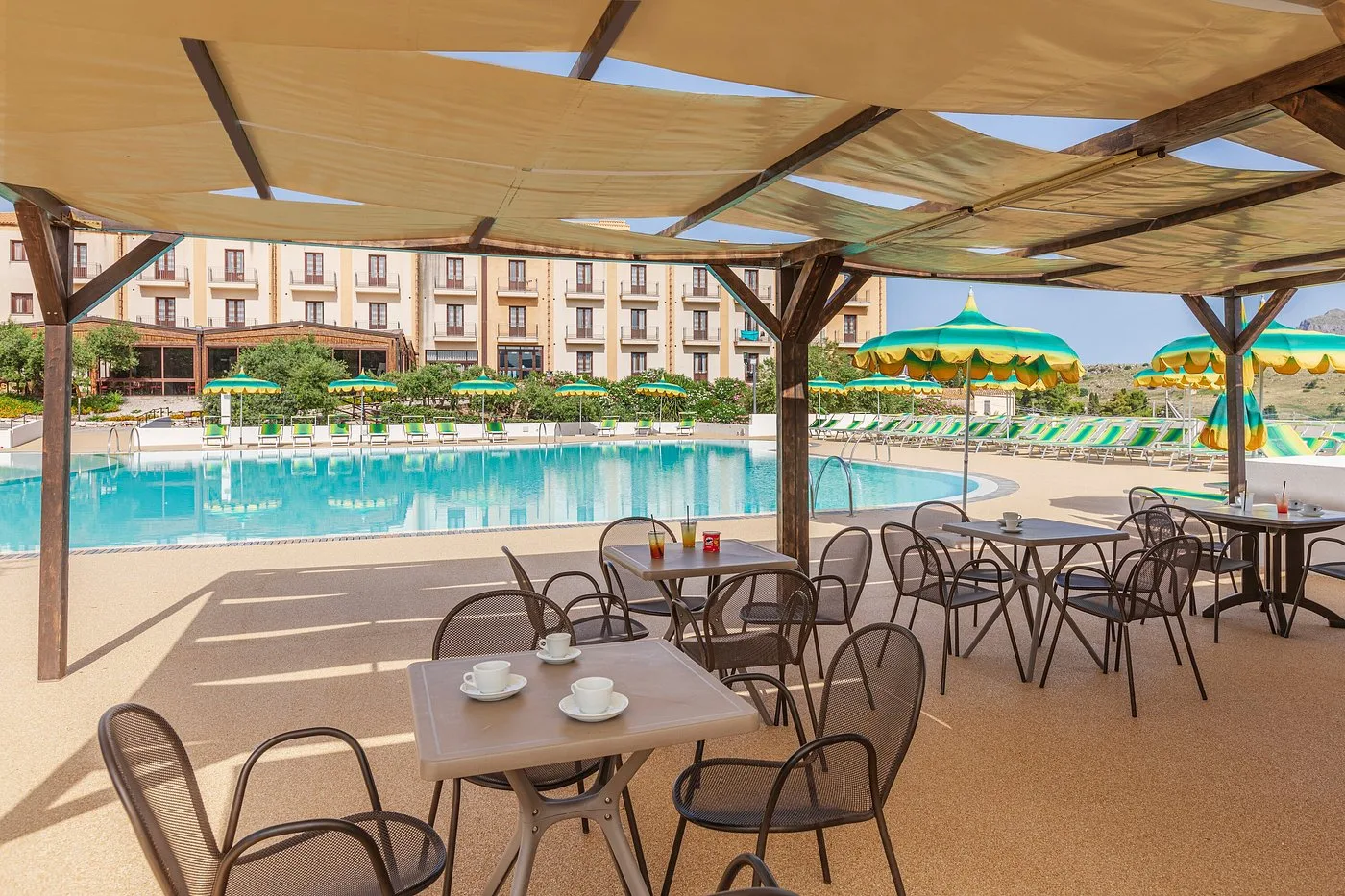 Area bar all'aperto con tavoli e sedie sotto pergolato affacciata sulla piscina