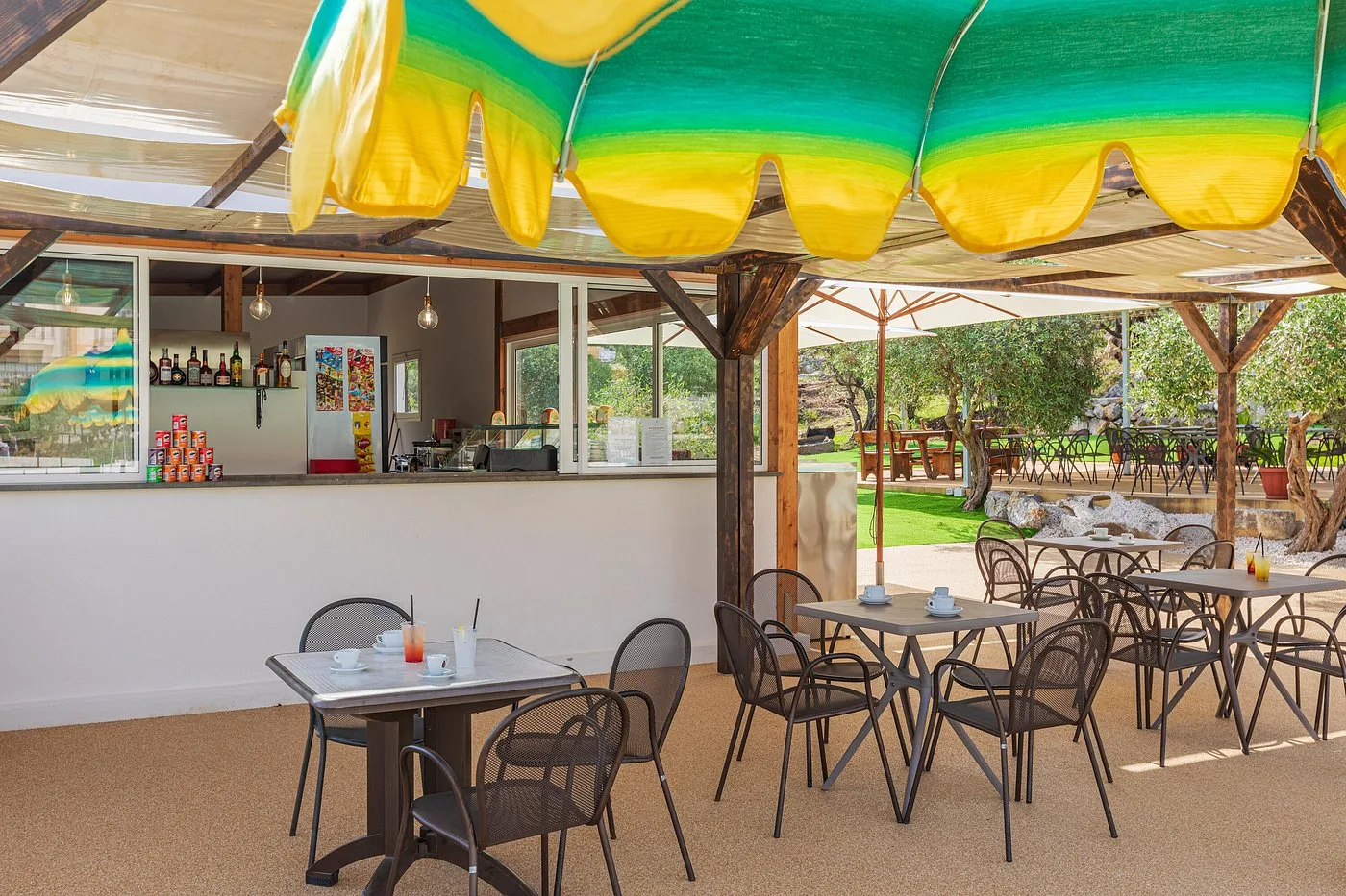Bar esterno a bordo piscina con bancone, tavoli e sedie sotto tende gialle e verdi