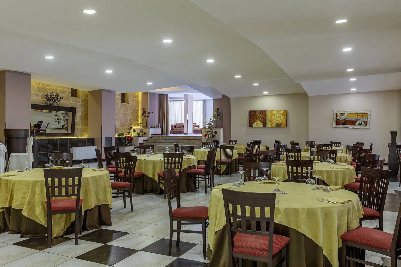 Sala ristorante interna con tavoli rotondi apparecchiati, sedie in legno e pavimento a scacchi
