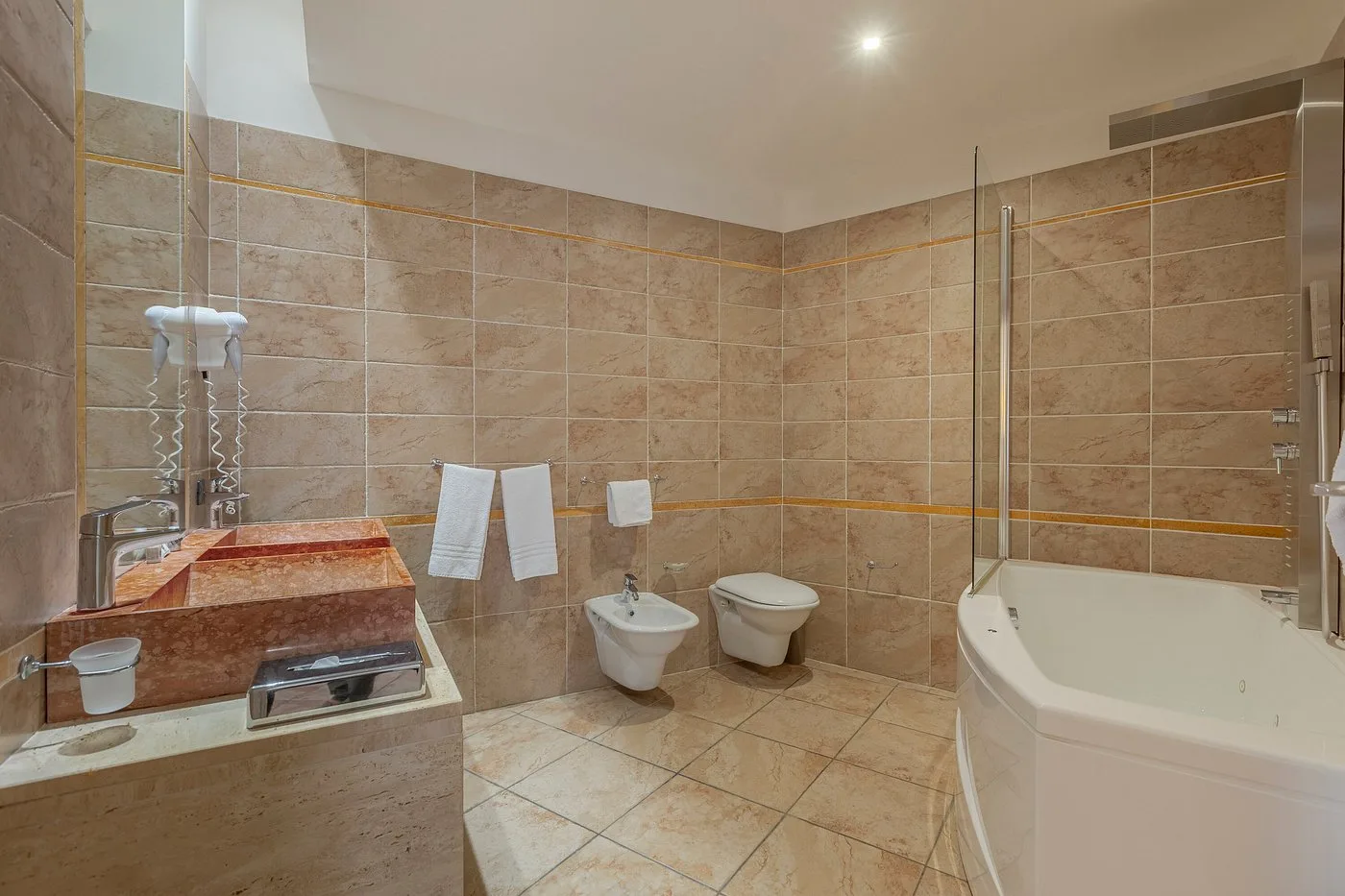 Bagno moderno con vasca idromassaggio angolare, lavabo in marmo rosso, bidet e WC
