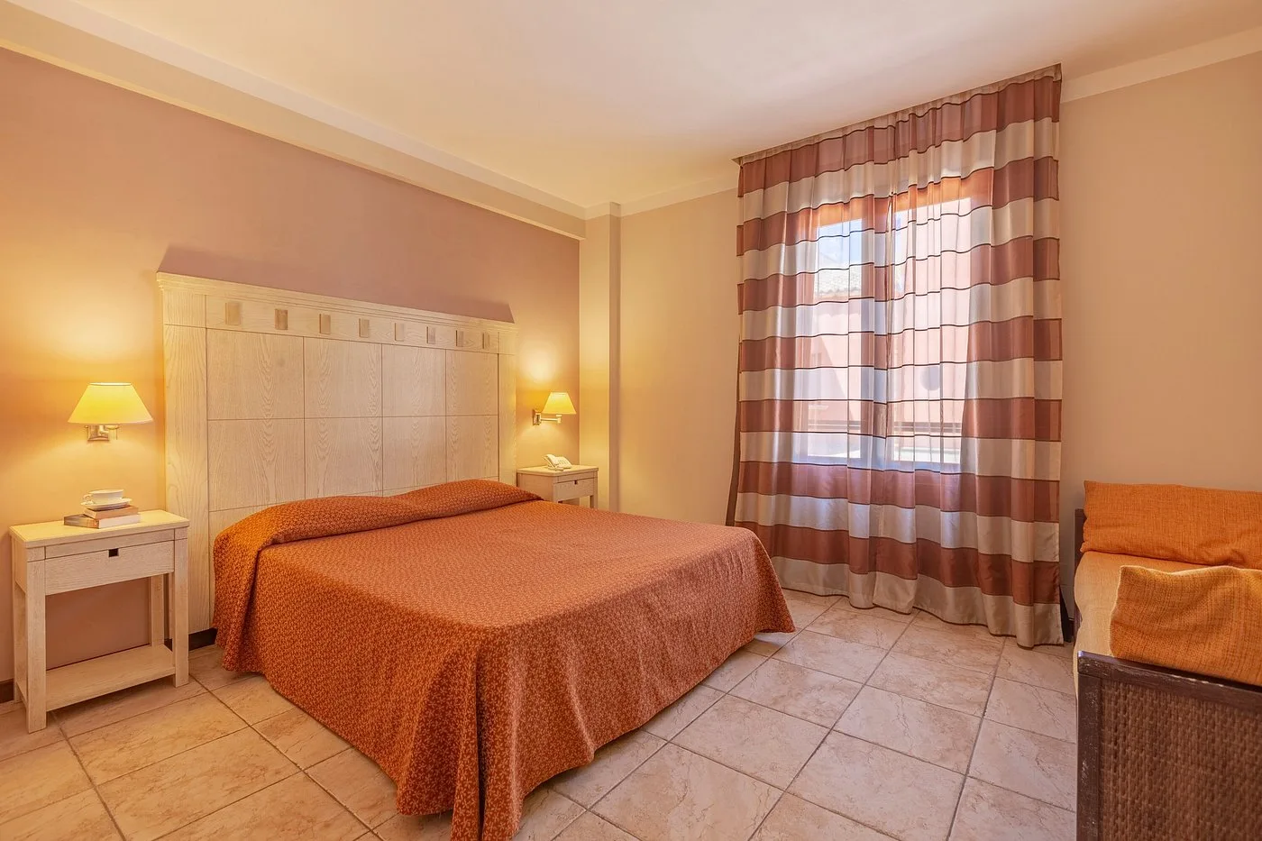 Camera matrimoniale con pareti color pesca, tende a righe e letto con copriletto arancione