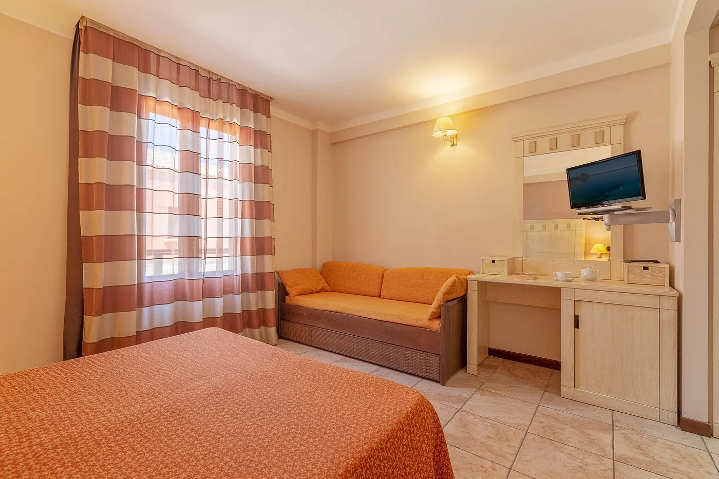 Camera con letto matrimoniale, divano arancione, scrivania e TV a parete