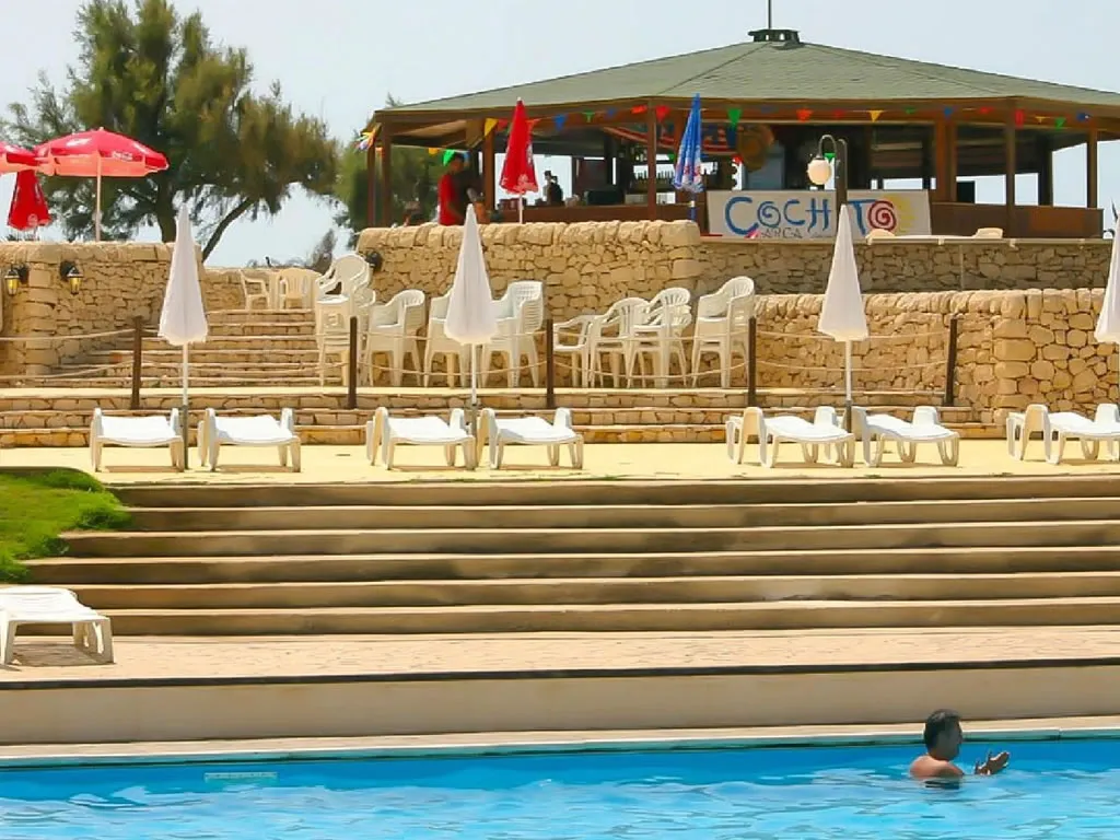 Bar a bordo piscina con lettini, ombrelloni e gradinate in pietra