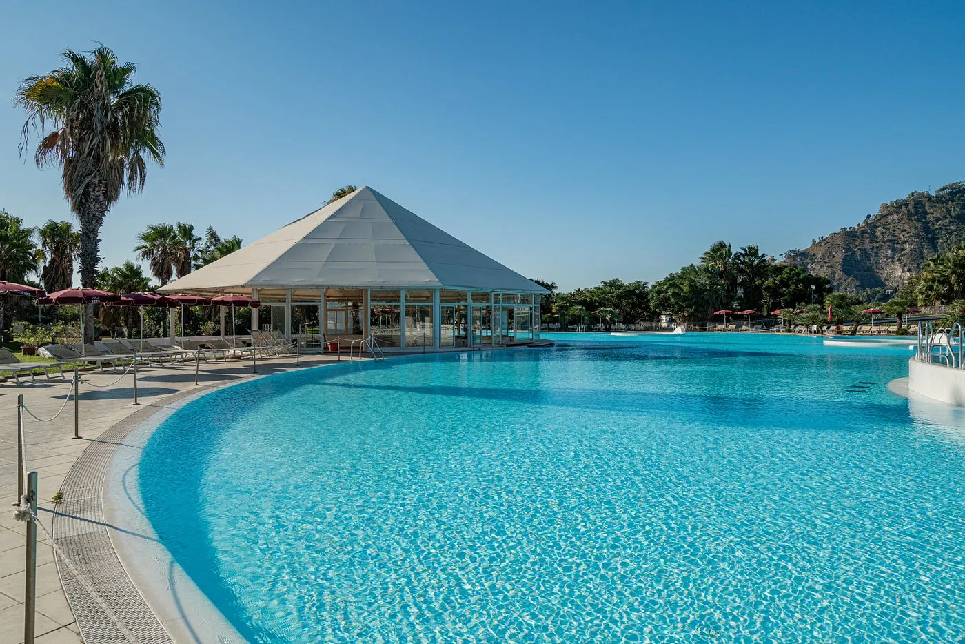 Piscina dalle acque cristalline con gazebo bianco e palme sotto il cielo azzurro