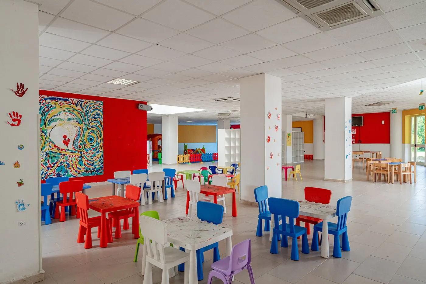 Sala interna per bambini con tavolini e sedie colorate e pareti dipinte
