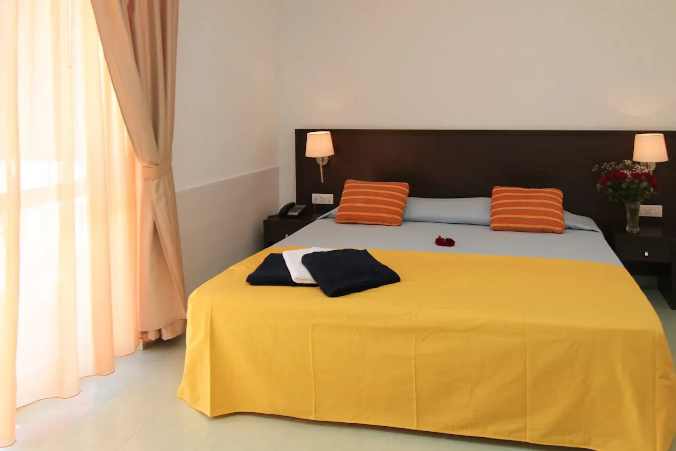 Camera matrimoniale con copriletto giallo, cuscini arancioni e tende chiare