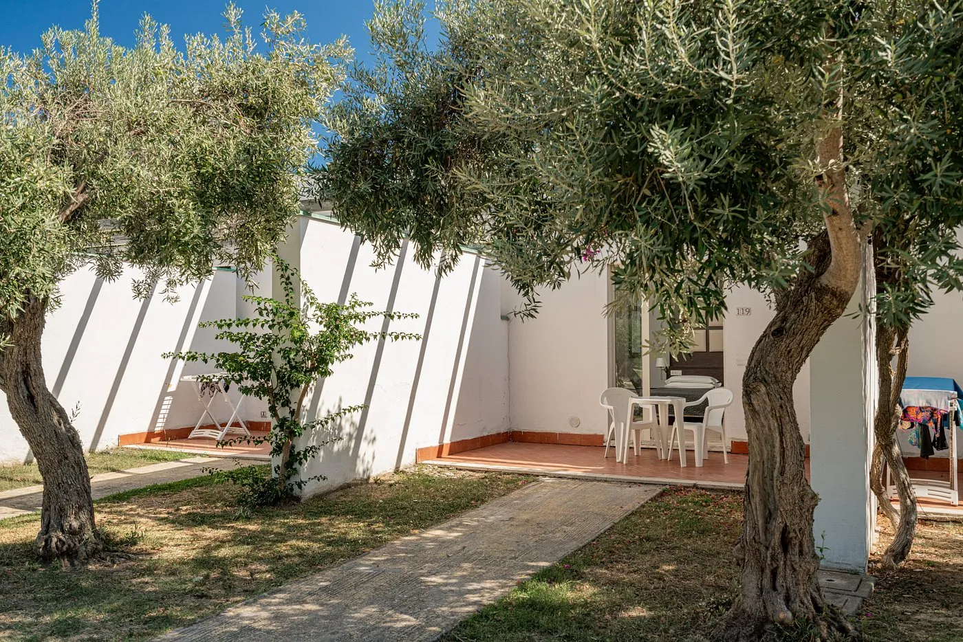 Veranda esterna di un bungalow con tavolino e sedie tra ulivi e giardino