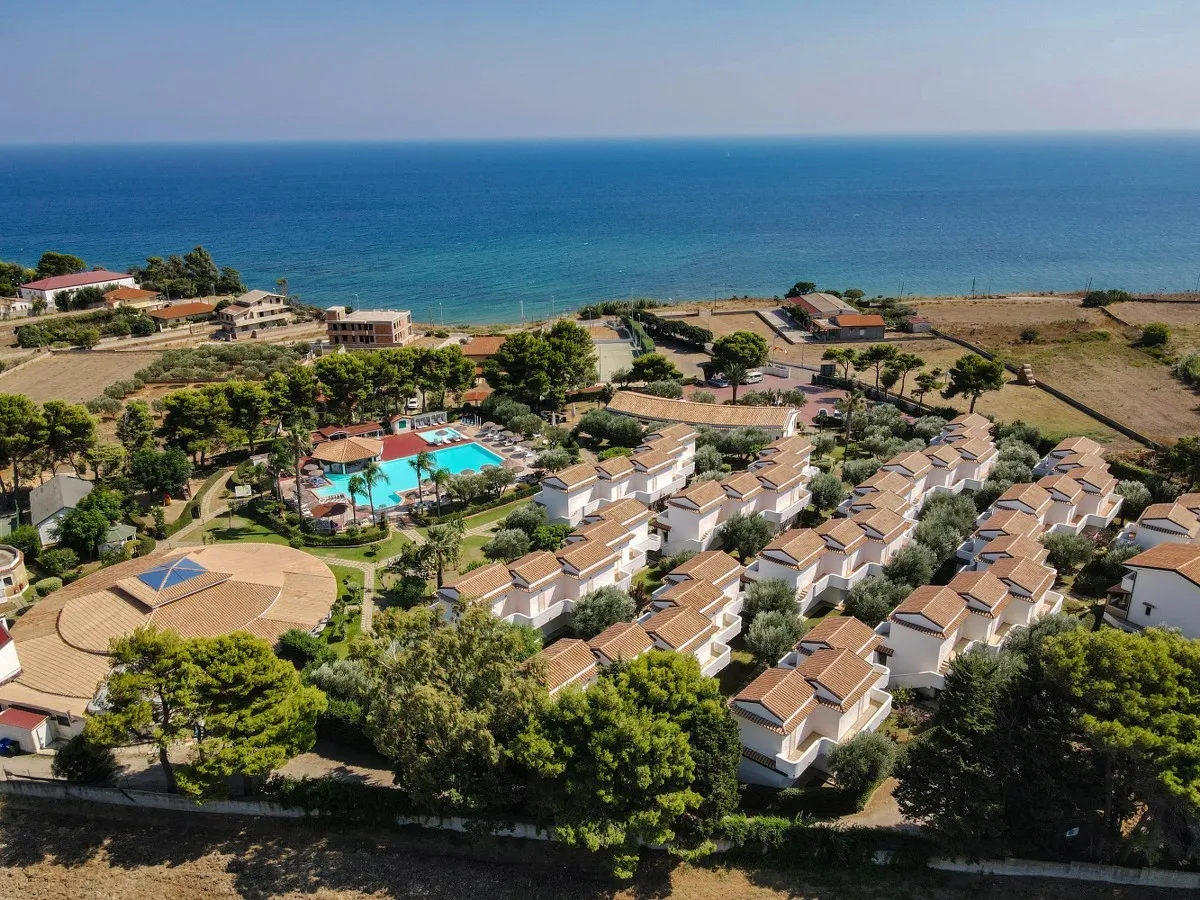 Vista aerea del villaggio turistico con villette, piscina e mare sullo sfondo