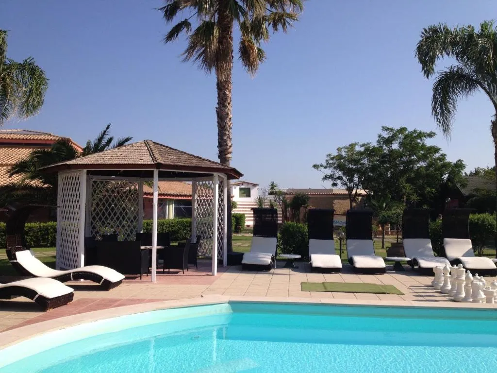 Area relax con lettini bianchi, gazebo e palme a bordo piscina