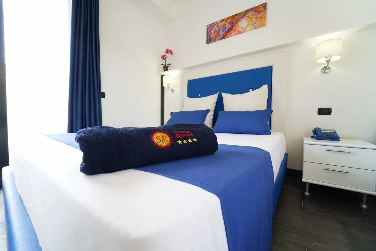 Camera matrimoniale con dettagli blu, comodino e telo brandizzato sul letto