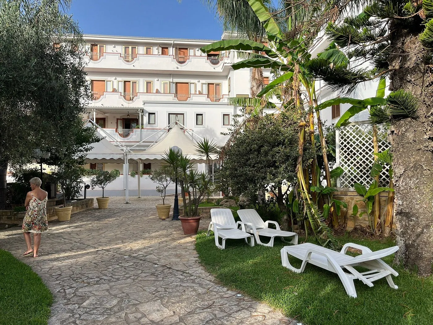 Giardino curato con lettini bianchi e vialetto in pietra davanti all'hotel