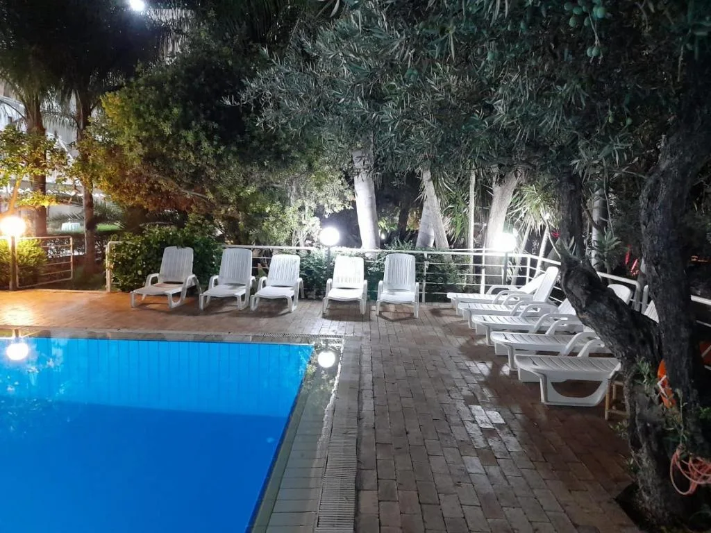 Area piscina con lettini bianchi tra alberi illuminati di sera