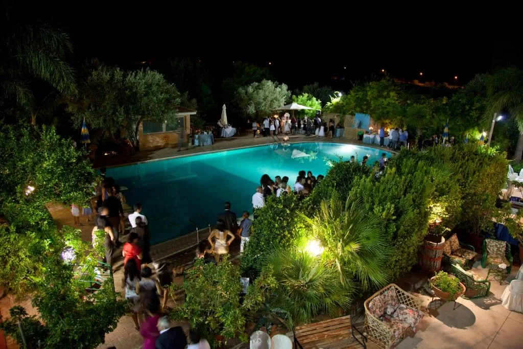 Festa serale a bordo piscina con ospiti tra la vegetazione illuminata